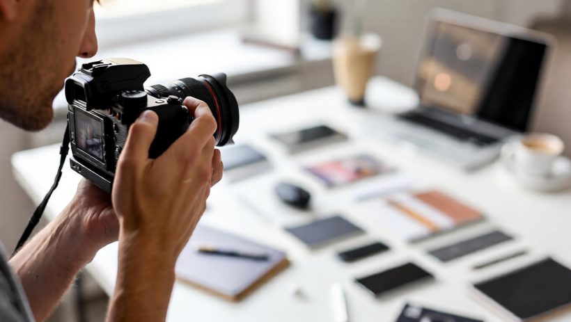Blogger taking high-quality flat lay photos using a mirrorless camera and natural window light in a home office.